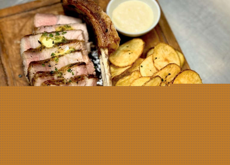 Signature tomahawk steak sliced on wooden board with crispy potato chips